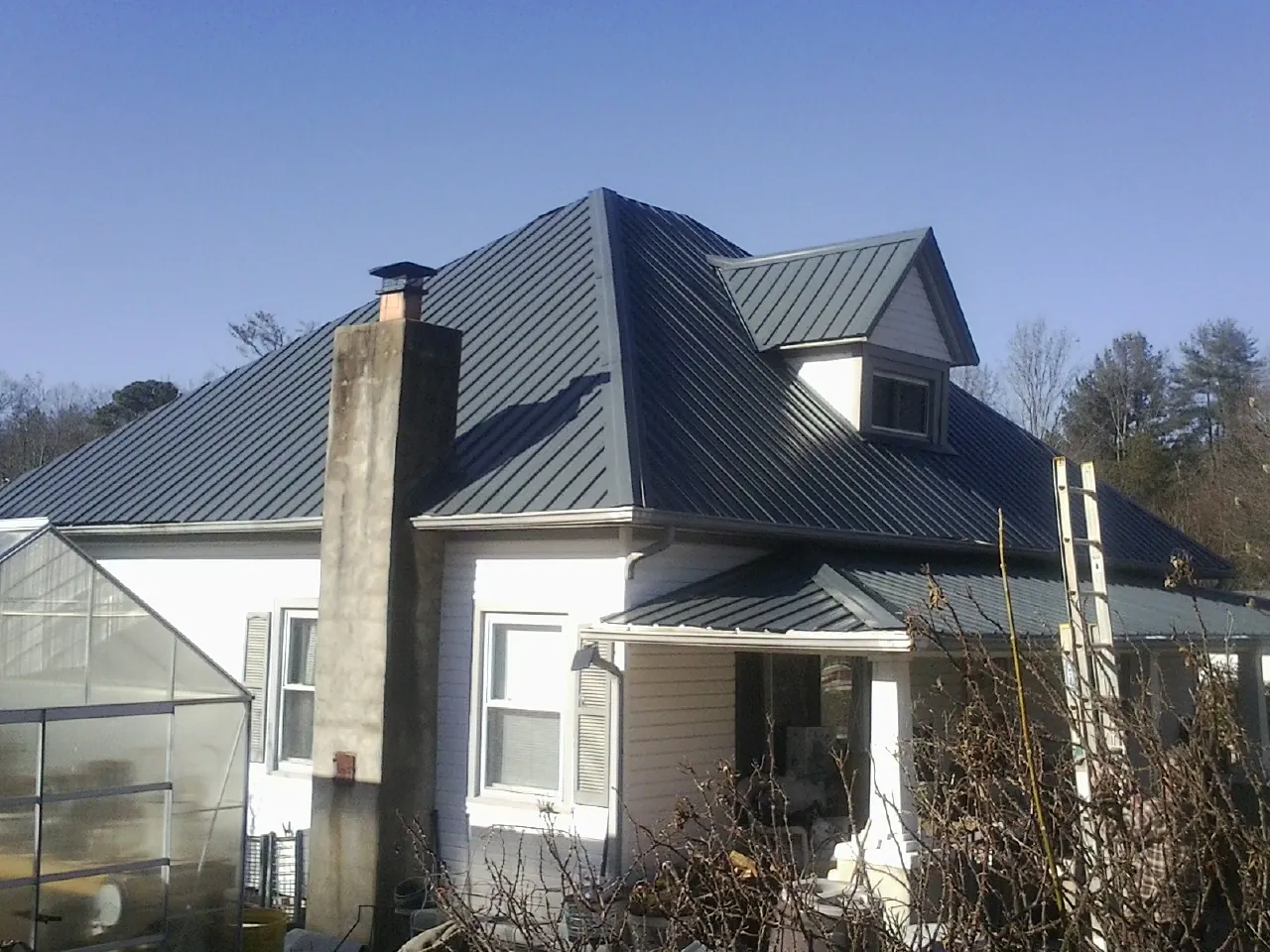 Dark blue standing seam metal roof on a white farmhouse with dormer — Slate & Tile Roof Repair by Roofing Brothers in Allegan