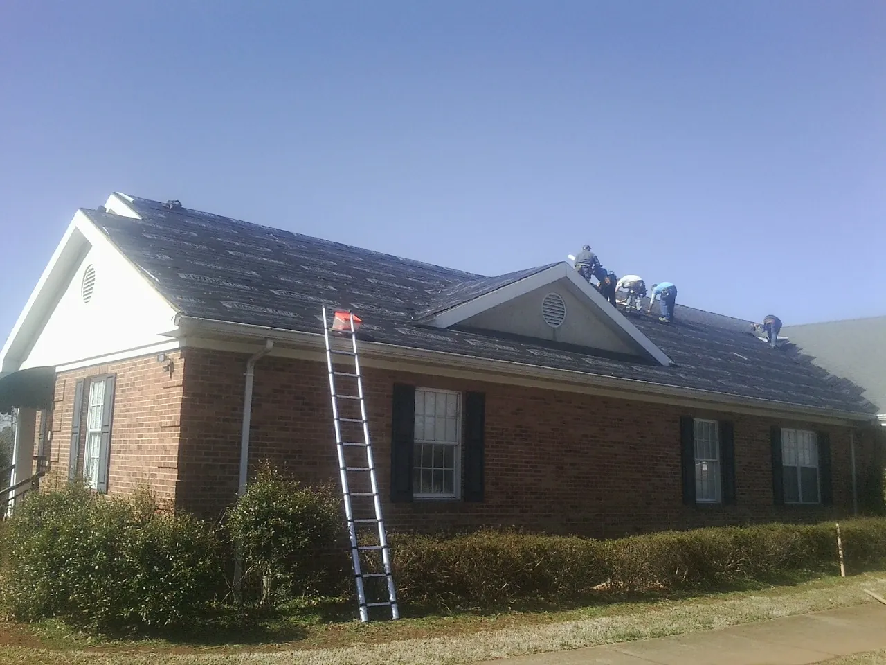Crew tearing shingles off a brick ranch roof with a ladder set — Metal Roof Repair work by our crew in Allegan