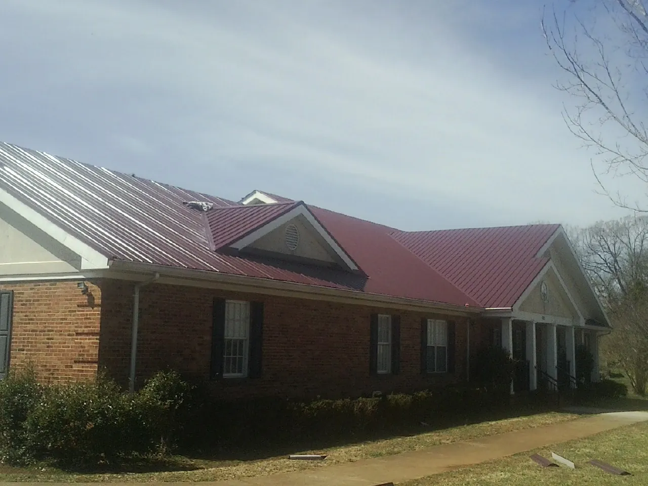 Red metal roof with gabled entries on a long brick building, from a Hail Damage Roof Repair job in Allegan
