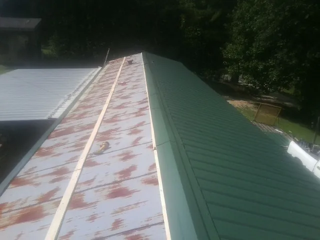 Old rusted panels beside newly installed green metal roofing — Wind Damage Roof Repair by Roofing Brothers in Allegan