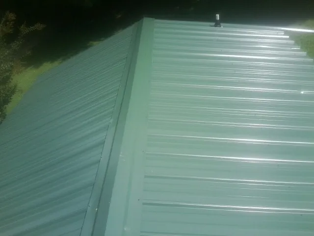 New green metal panels meeting at the ridge of a roof — Flat Roof Repair work by our crew in Allegan