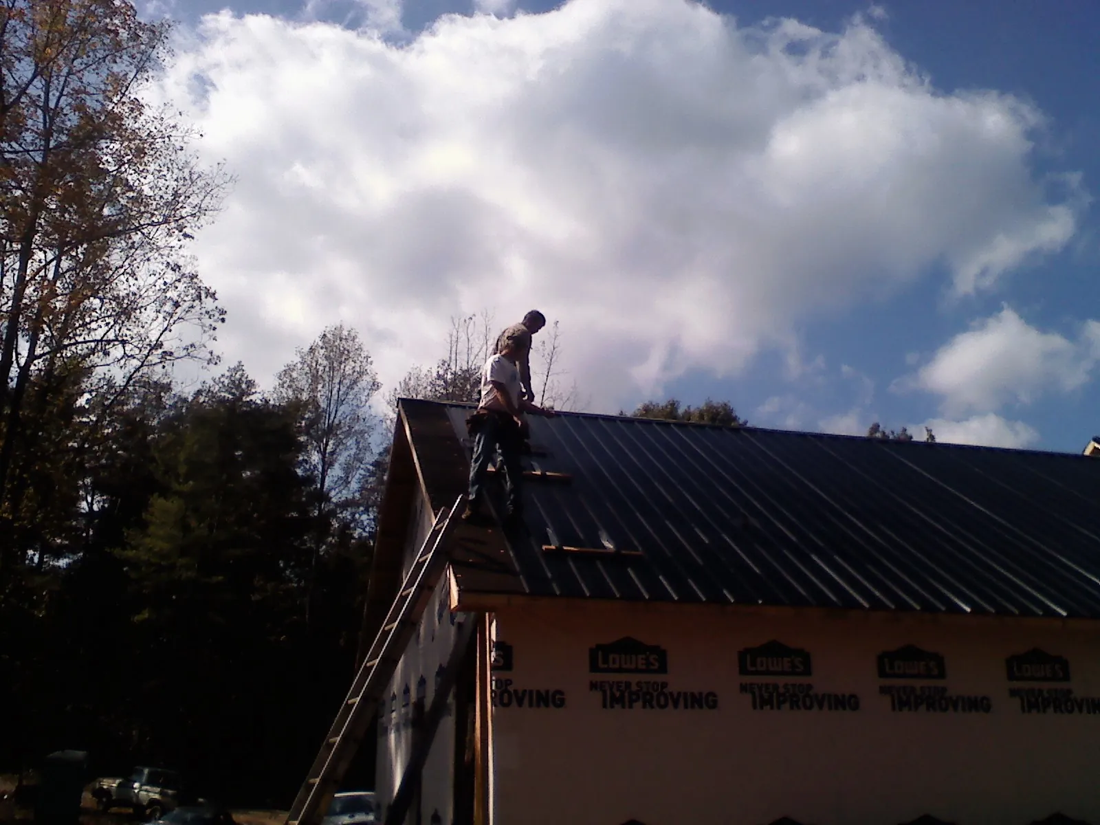 Roofer fastening dark metal panels high against a cloudy sky, from a Roof Inspection job in Allegan