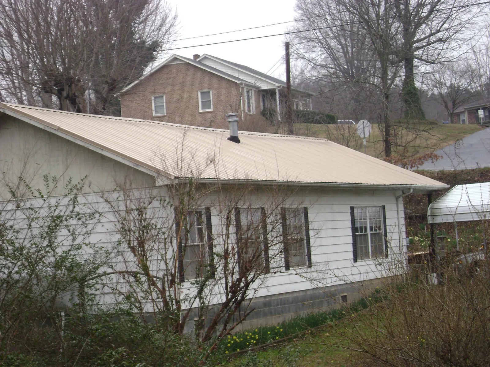 Tan metal roof on a white sided house set into a hillside — Commercial Roofing by Roofing Brothers in Allegan