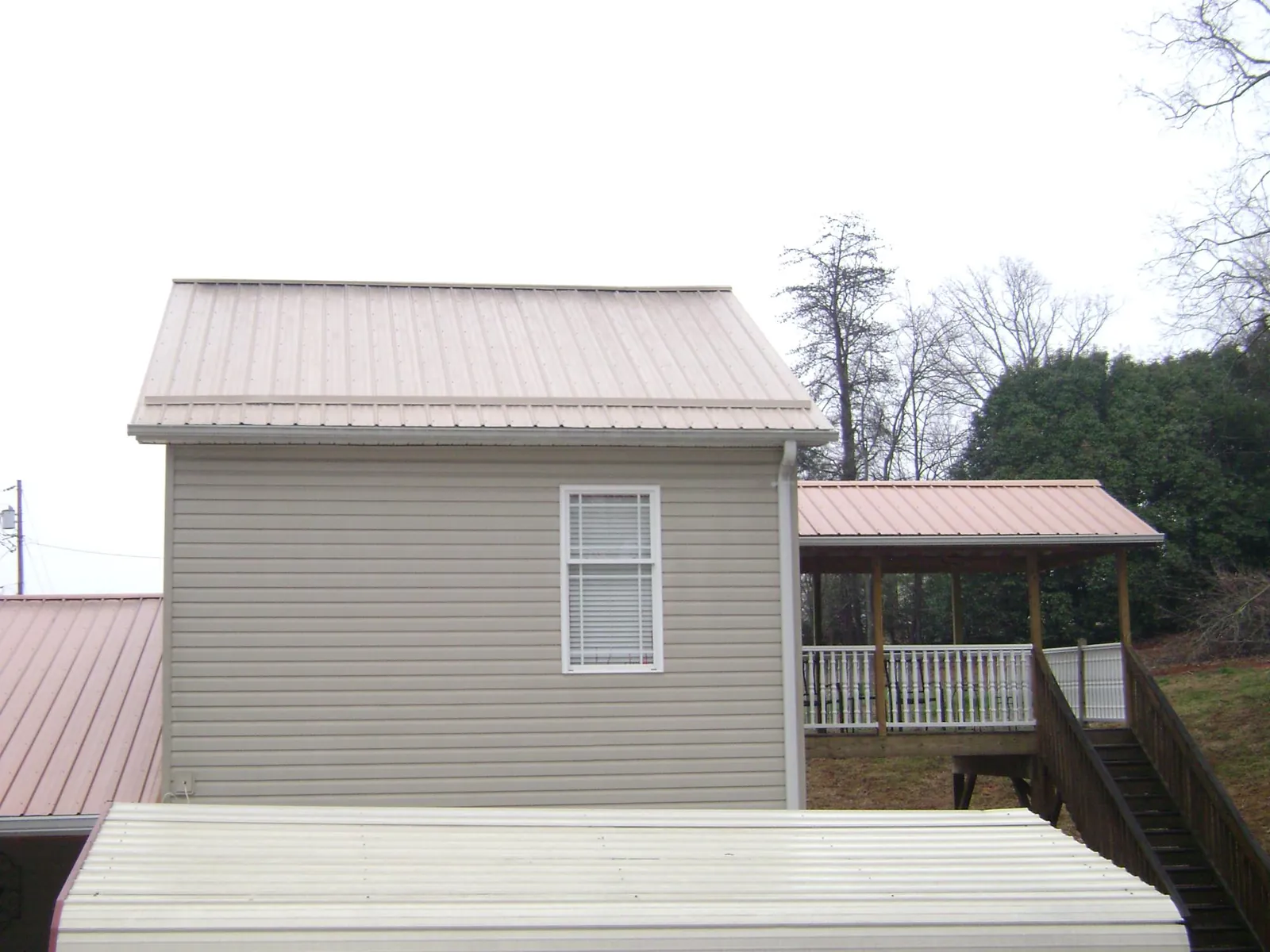 Tan metal roofs on a two story addition and attached porch, from a Roof Replacement job in Allegan